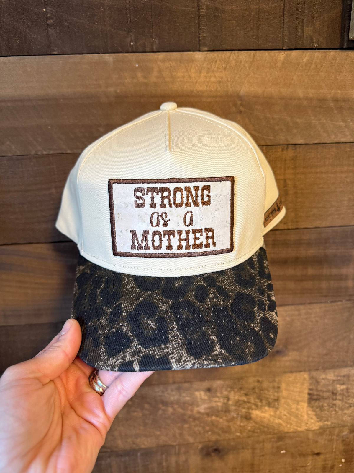 Cap with 'Strong as a Mother' text held against a wooden background